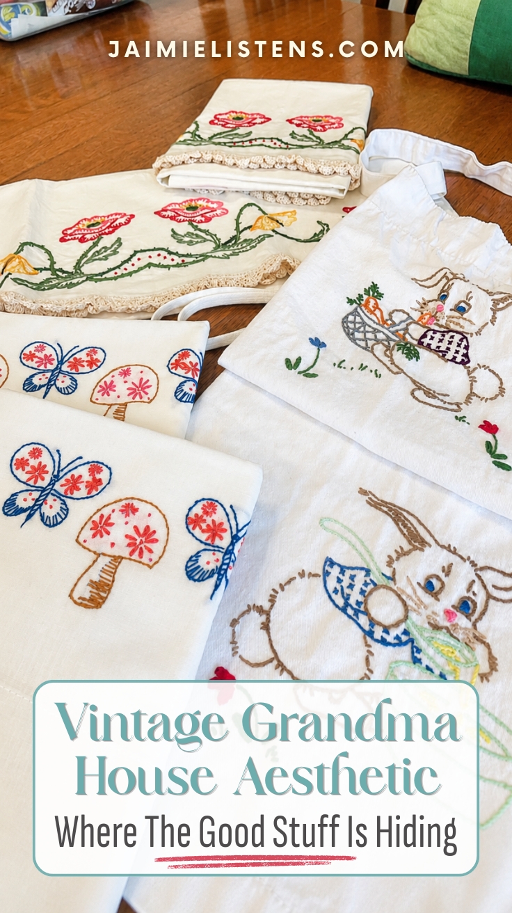 Vintage embroidered linens, bunny apron, and handmade textiles displayed on a wooden table. Pin text reads: Where The Good Stuff Is Hiding.