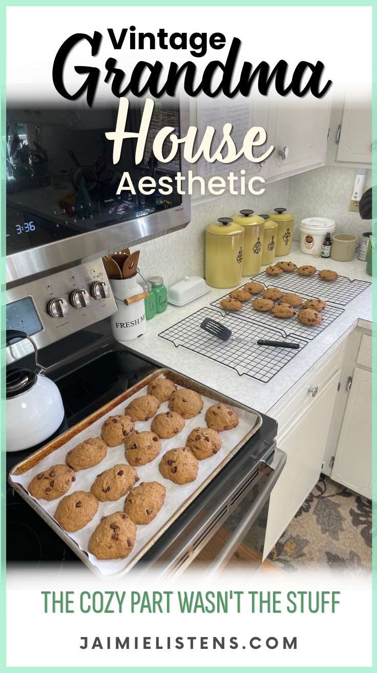 Fresh chocolate chip cookies cooling on baking racks in a vintage-inspired kitchen with yellow canisters and baking tools. Pin text reads: The Cozy Part Wasn't The Stuff.