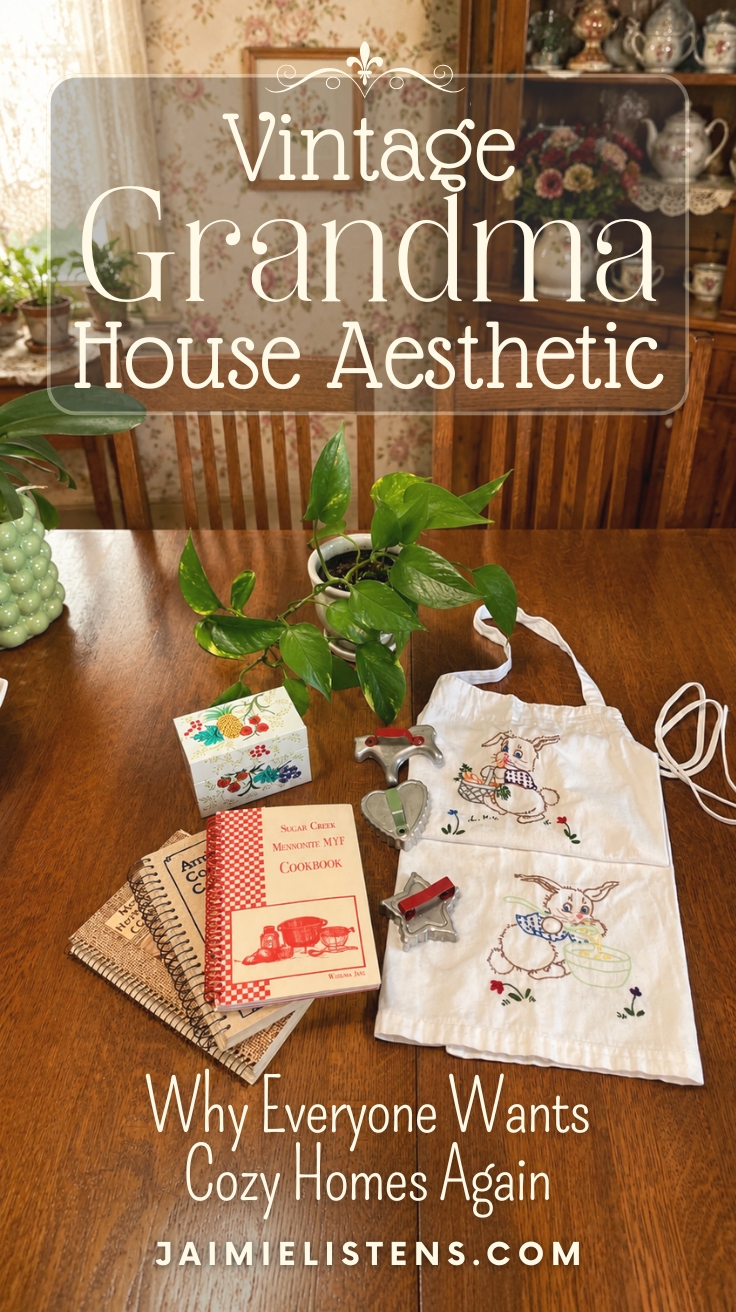 Vintage grandma house aesthetic kitchen with embroidered bunny apron, church cookbooks, recipe box, cookie cutters, and houseplants arranged on a wooden table. Pin text reads: Why Everyone Wants Cozy Homes Again.