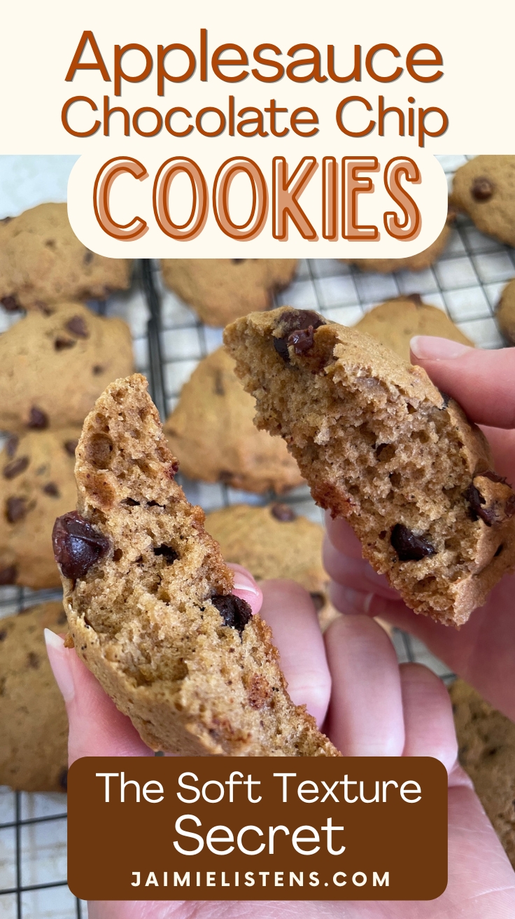 Broken applesauce chocolate chip cookie showing the soft, cake-like interior texture with cooling cookies in the background.